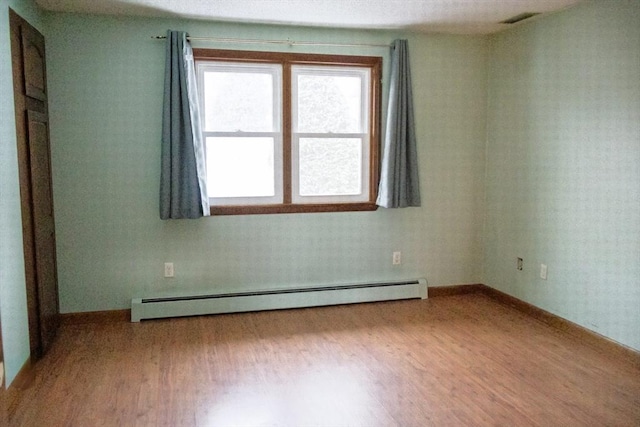 spare room with baseboard heating, wood finished floors, visible vents, and baseboards