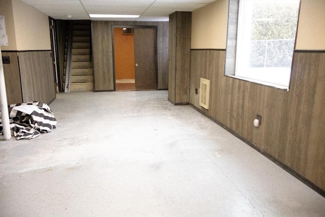 empty room featuring a paneled ceiling, wooden walls, and wainscoting