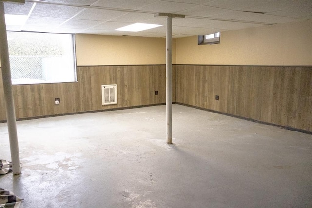 basement featuring plenty of natural light, a paneled ceiling, a wainscoted wall, and wood walls