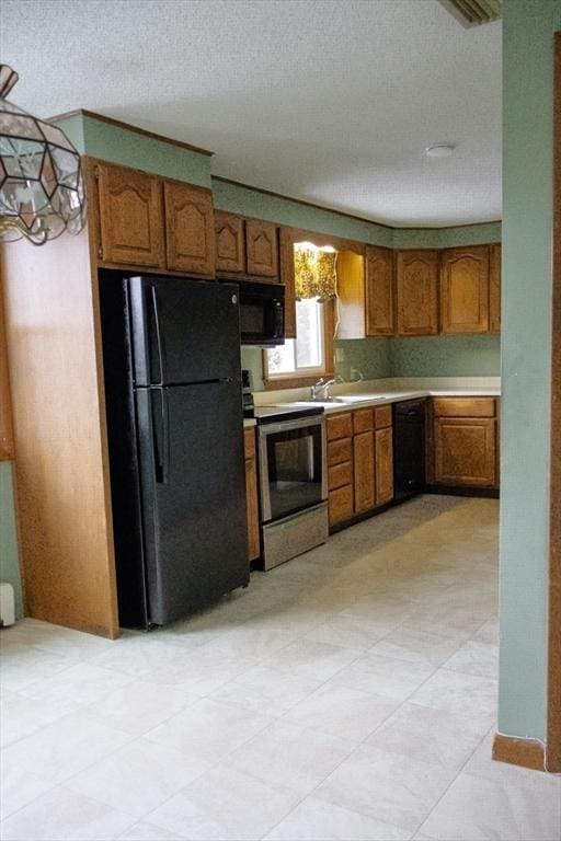 kitchen with a textured ceiling, black appliances, light countertops, and brown cabinets