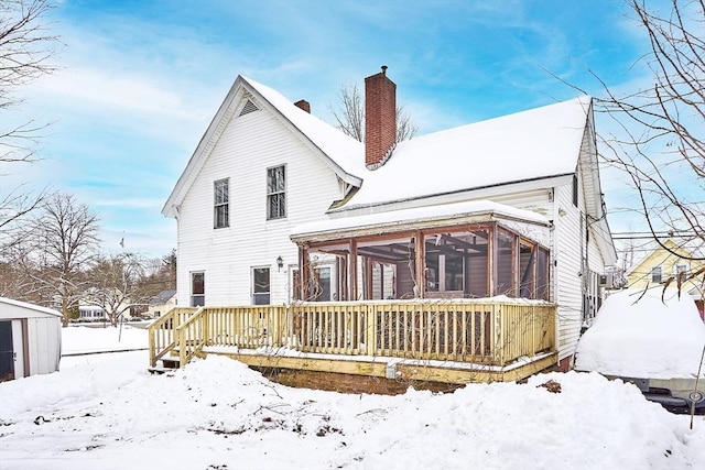 snow covered house featuring a wooden deck and a sunroom