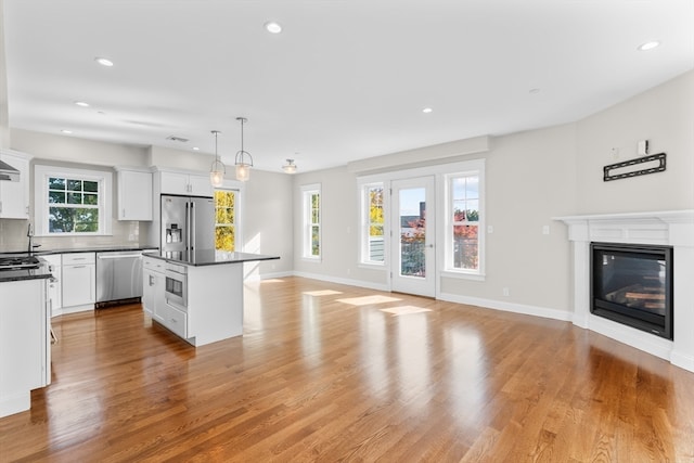 kitchen with hanging light fixtures, appliances with stainless steel finishes, white cabinetry, light wood-type flooring, and a center island