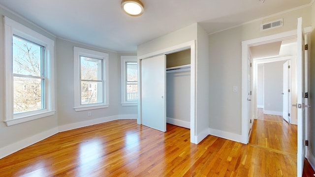 unfurnished bedroom featuring light hardwood / wood-style floors, ornamental molding, and a closet