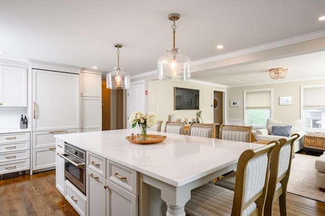 kitchen with stainless steel oven, open floor plan, light countertops, ornamental molding, and white cabinets