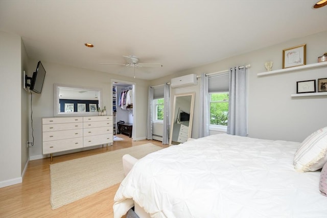 bedroom with a wall mounted air conditioner, light wood-style flooring, baseboards, and ceiling fan