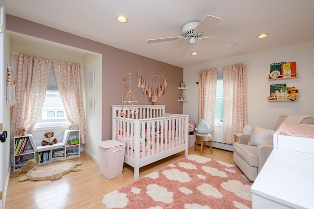 bedroom featuring wood finished floors, recessed lighting, a crib, a baseboard heating unit, and a ceiling fan