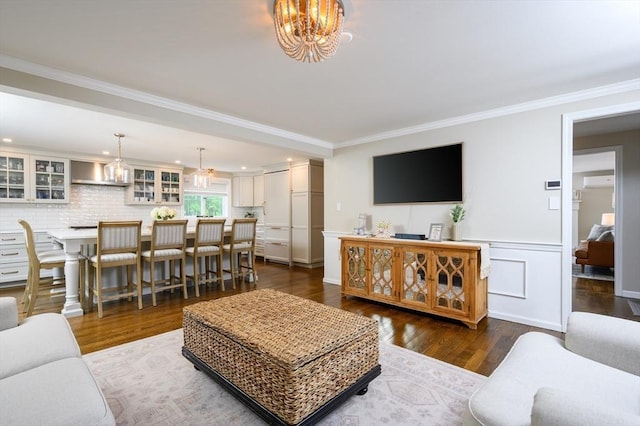 living area with a chandelier, crown molding, dark wood-style flooring, a wall mounted air conditioner, and wainscoting