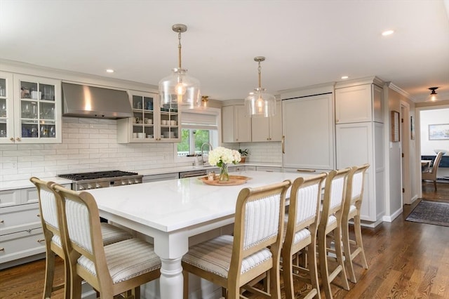 kitchen with wall chimney range hood, tasteful backsplash, stainless steel gas stovetop, a breakfast bar, and dark wood-style flooring