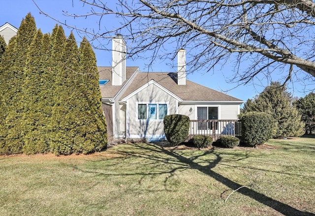 cape cod house featuring roof with shingles, a chimney, a front lawn, and a wooden deck