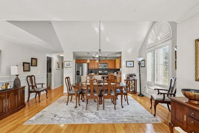 dining area featuring vaulted ceiling, a wainscoted wall, light wood-style flooring, and a notable chandelier