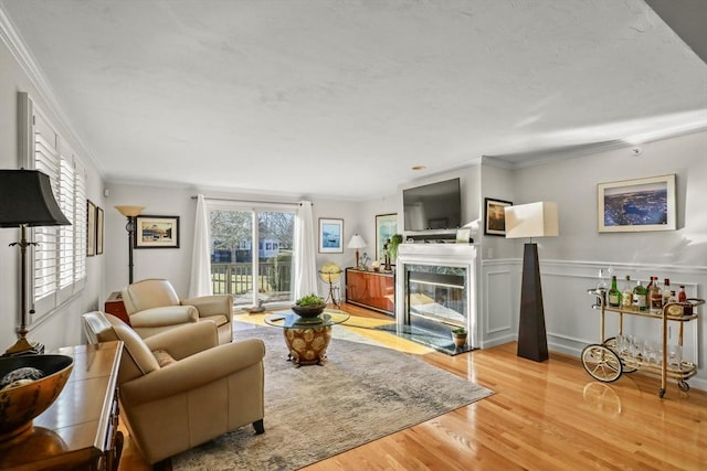 living room with ornamental molding, light wood-type flooring, wainscoting, and a premium fireplace