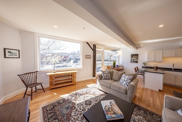 living room with beamed ceiling, light hardwood / wood-style flooring, sink, and a wealth of natural light