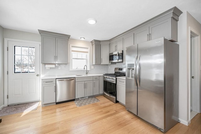 kitchen with tasteful backsplash, light countertops, appliances with stainless steel finishes, a sink, and light wood-type flooring