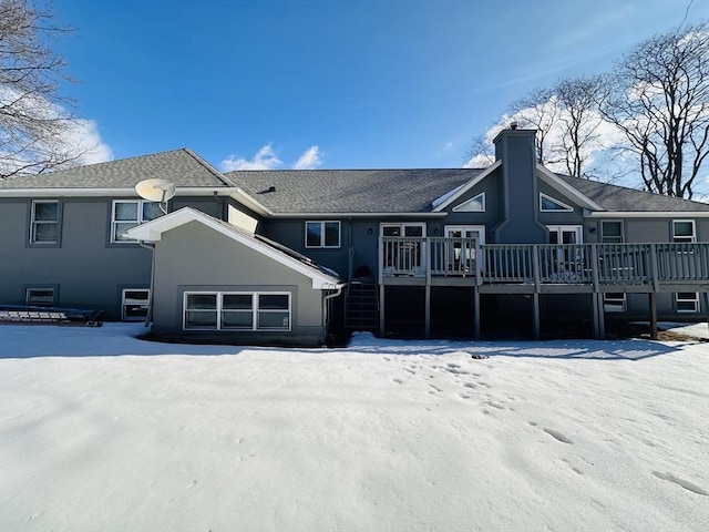 snow covered property with stucco siding, a chimney, and a wooden deck