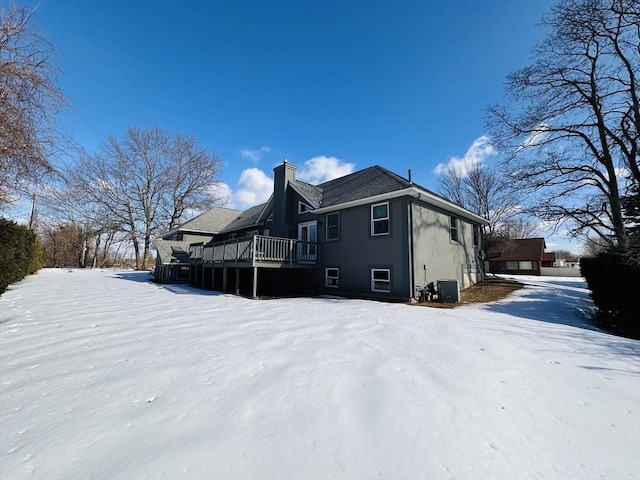 view of snowy exterior featuring a deck, central AC unit, and a chimney