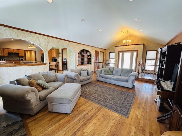 living room featuring arched walkways, built in features, vaulted ceiling, light wood-type flooring, and a chandelier