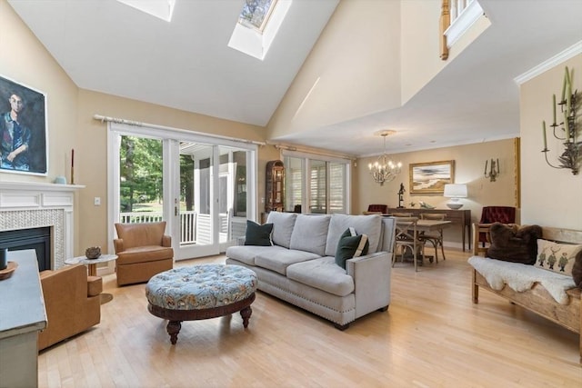 living room featuring a tile fireplace, lofted ceiling with skylight, a chandelier, and light hardwood / wood-style floors