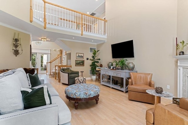 living room with french doors, a towering ceiling, a fireplace, and light hardwood / wood-style floors