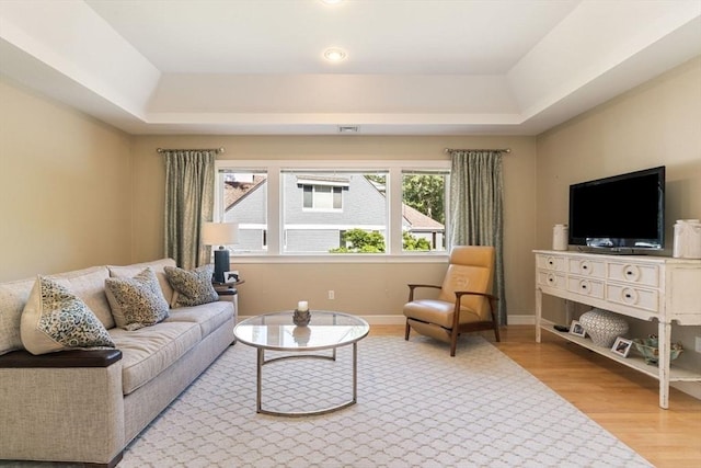 living room with a tray ceiling and light wood-type flooring