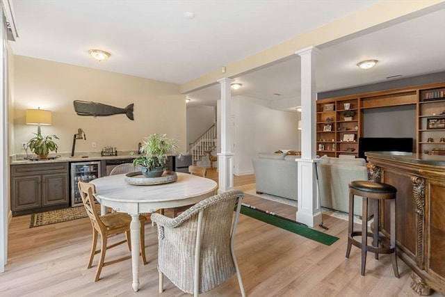 dining area featuring bar area, beverage cooler, decorative columns, and light wood-type flooring