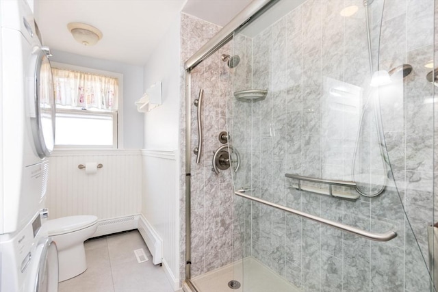 bathroom featuring a stall shower, tile patterned flooring, stacked washer / drying machine, wainscoting, and toilet