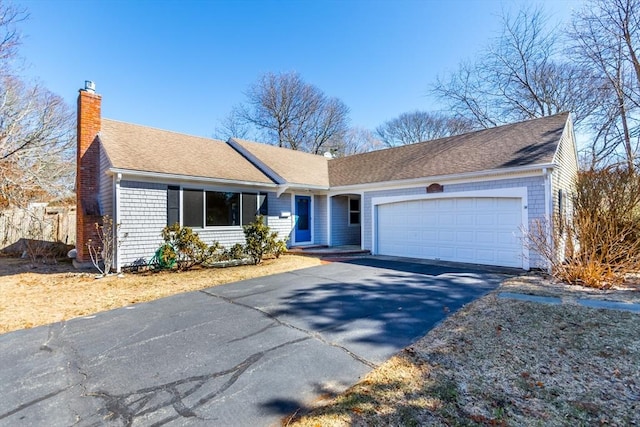 ranch-style home featuring driveway, an attached garage, a chimney, and a shingled roof