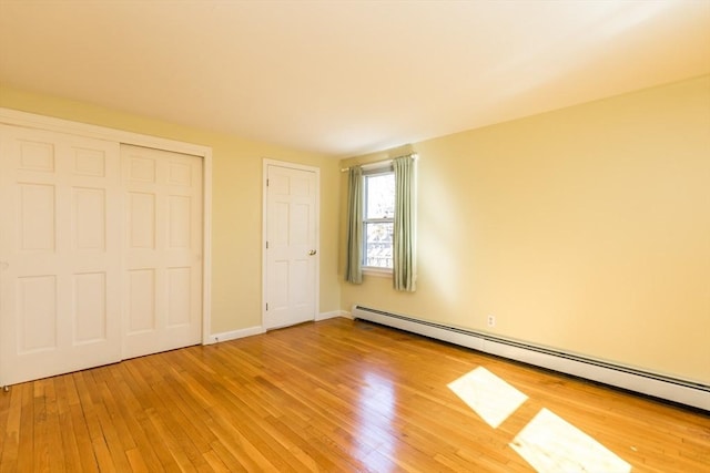 unfurnished bedroom with light wood finished floors, baseboards, a baseboard heating unit, and a closet