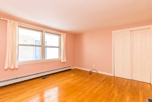 unfurnished bedroom with visible vents, light wood-style flooring, a baseboard heating unit, a closet, and baseboards