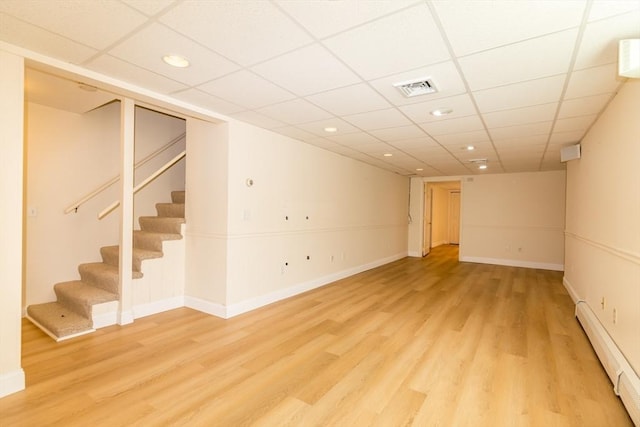 finished basement with visible vents, baseboards, stairway, light wood-type flooring, and baseboard heating