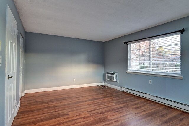 spare room featuring a wall unit AC, a baseboard radiator, a textured ceiling, and dark hardwood / wood-style flooring