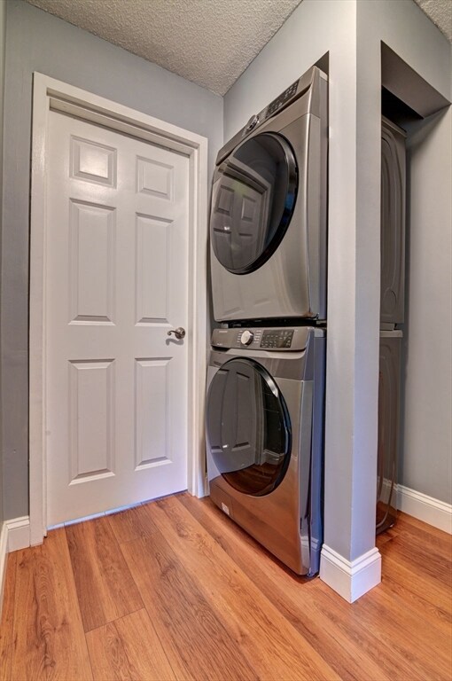 washroom with stacked washer and dryer, a textured ceiling, and light wood-type flooring