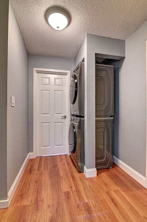 laundry room with stacked washer and dryer, wood-type flooring, and a textured ceiling