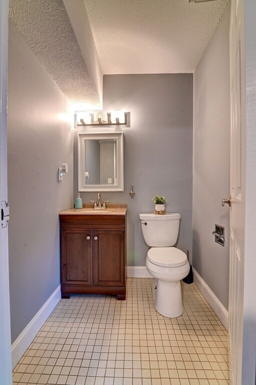 bathroom with toilet, vanity, a textured ceiling, and tile patterned floors