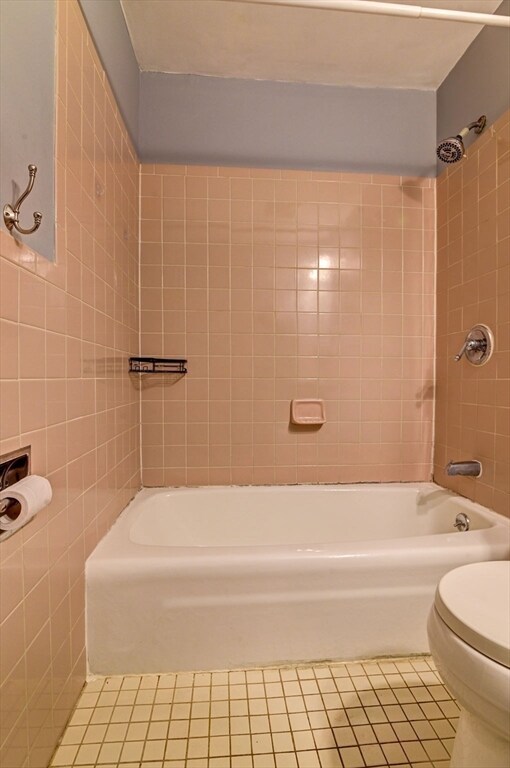 bathroom with tile walls, tiled shower / bath, tile patterned floors, and toilet