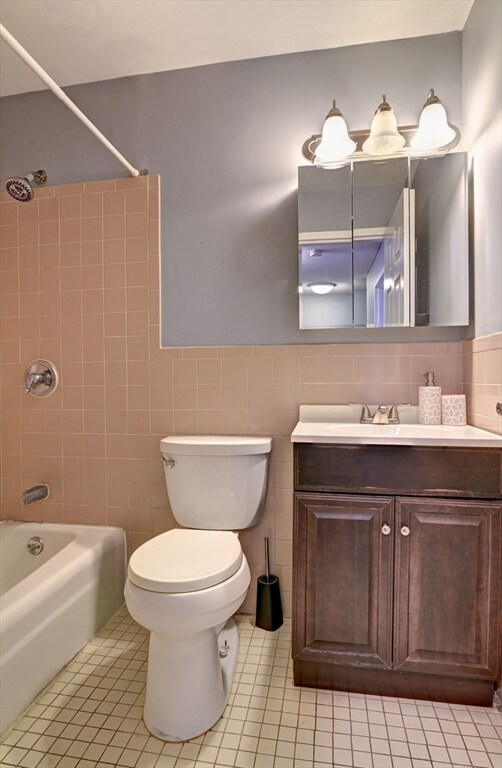 full bathroom with tile patterned flooring, toilet, tile walls, and tiled shower / bath combo