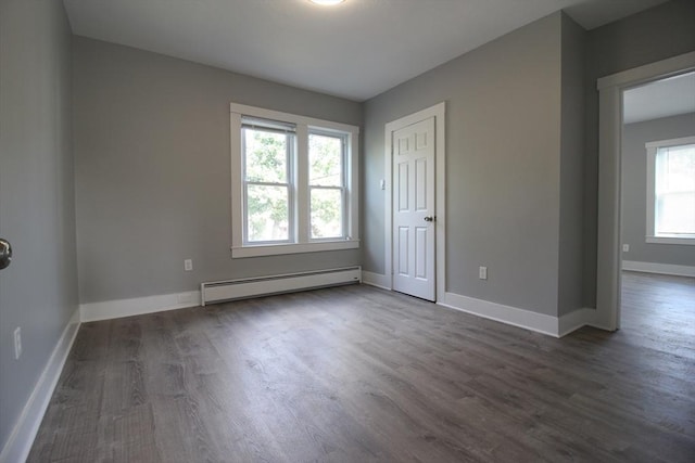 unfurnished room with plenty of natural light, dark wood-style flooring, and a baseboard heating unit