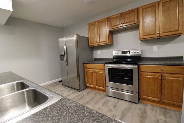 kitchen featuring brown cabinets, appliances with stainless steel finishes, light wood finished floors, and dark countertops