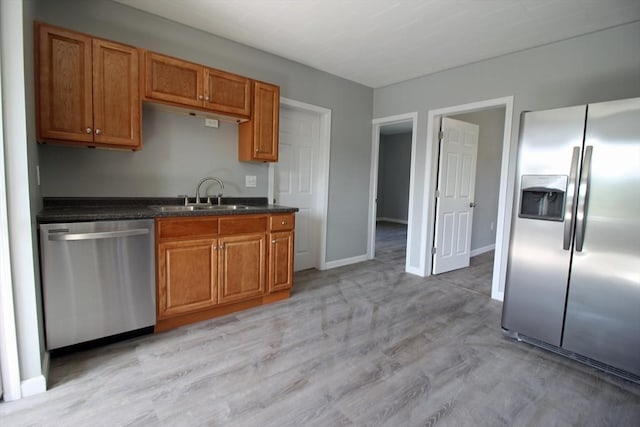 kitchen featuring brown cabinetry, dark countertops, a sink, stainless steel appliances, and light wood finished floors