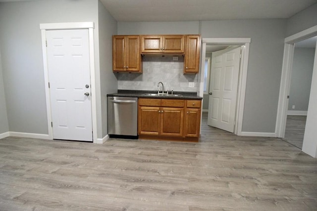 kitchen with baseboards, a sink, dark countertops, stainless steel dishwasher, and decorative backsplash
