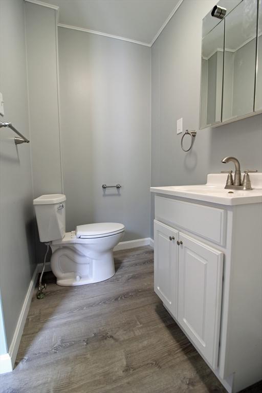 half bath featuring vanity, ornamental molding, toilet, wood finished floors, and baseboards