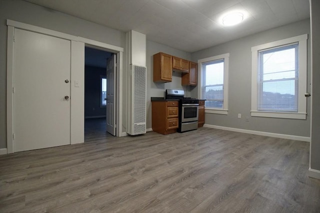 kitchen with brown cabinetry, stainless steel range with gas stovetop, dark countertops, and plenty of natural light