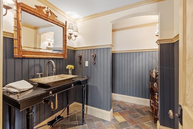 bathroom featuring stone tile floors, ornamental molding, a wainscoted wall, and a sink