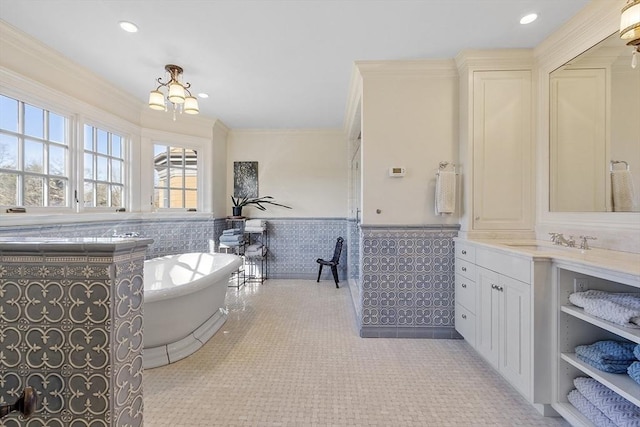 full bath featuring a freestanding tub, a wainscoted wall, an inviting chandelier, crown molding, and vanity