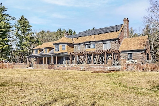 back of property with a lawn, solar panels, a chimney, and a pergola