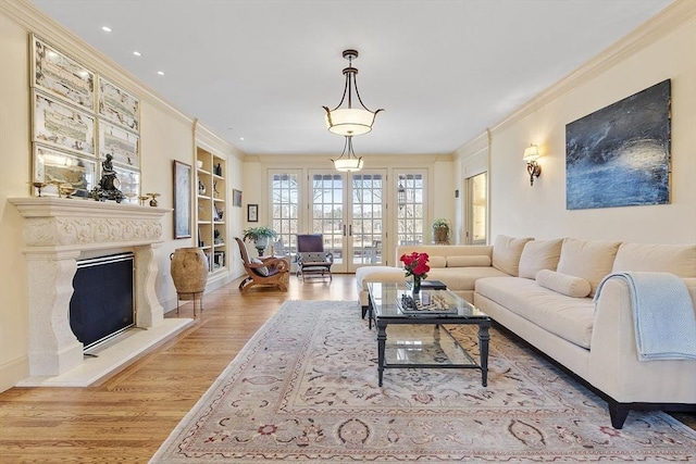 living area with a fireplace with raised hearth, built in features, ornamental molding, french doors, and wood finished floors