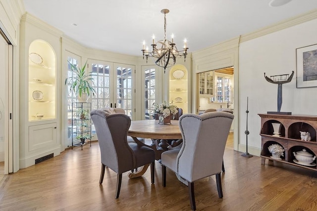 dining room with visible vents, a chandelier, ornamental molding, french doors, and wood finished floors