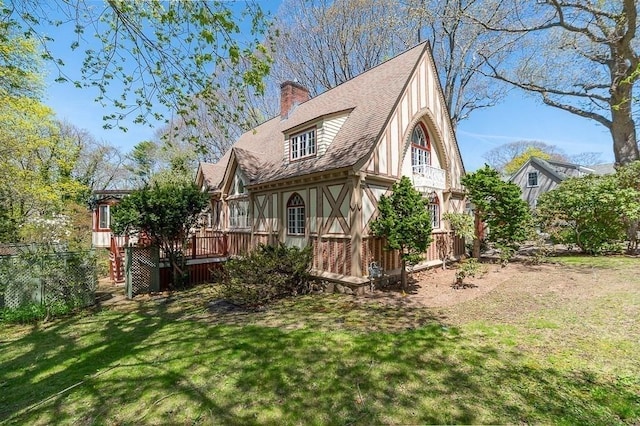 back of property featuring a chimney, a lawn, a deck, and roof with shingles