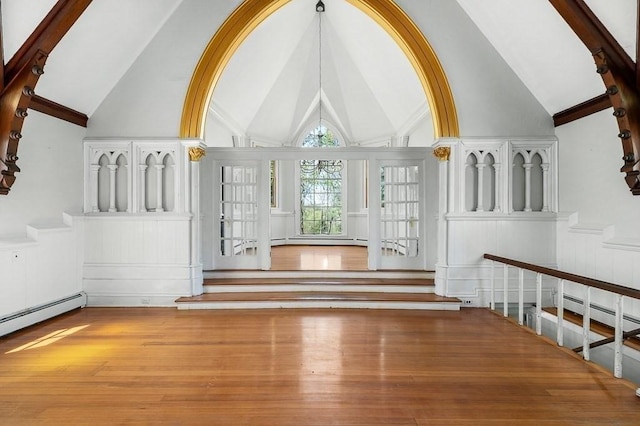 unfurnished living room featuring a decorative wall, stairway, high vaulted ceiling, a wainscoted wall, and wood finished floors