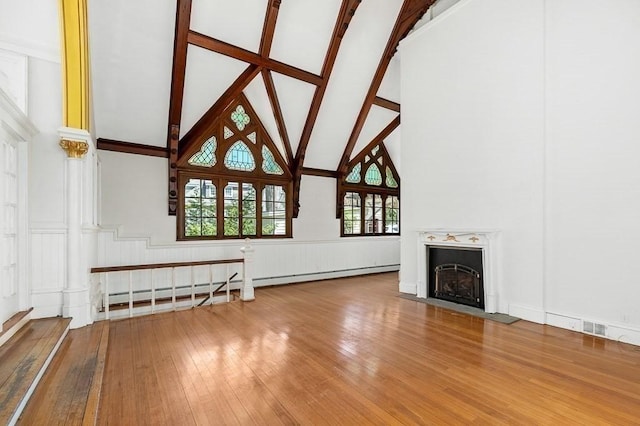 unfurnished living room with high vaulted ceiling, hardwood / wood-style floors, a wainscoted wall, a fireplace with flush hearth, and a decorative wall