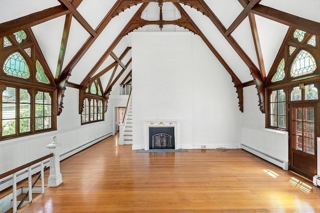 unfurnished living room with a baseboard radiator, high vaulted ceiling, light wood finished floors, wainscoting, and a fireplace with flush hearth